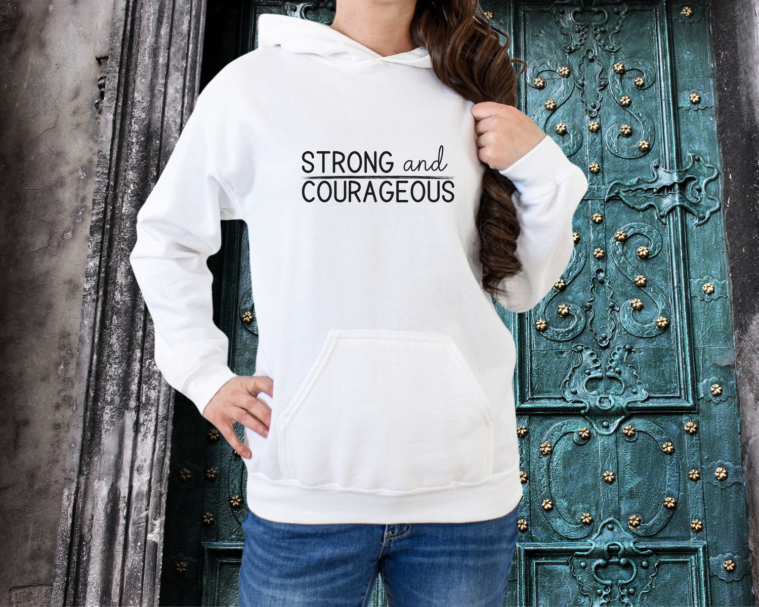 Woman wearing a white hoodie that states "Strong and Courageous" on the front.