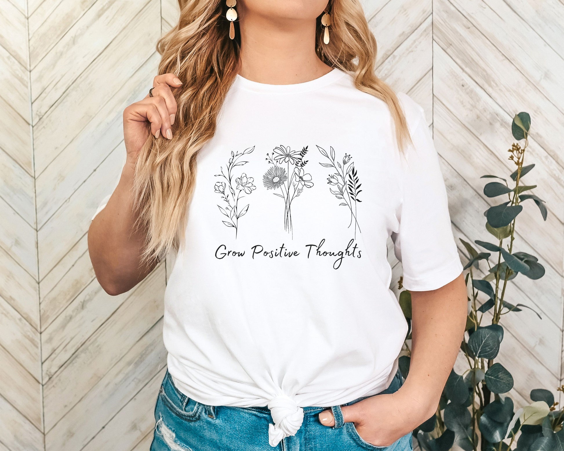 "Grow Positive Thoughts" t-shirt featuring black botanical floral illustrations and an uplifting message in elegant script. Available in white, ash, peach, red, and pink. Soft, lightweight fabric, perfect for spreading positivity and encouragement.