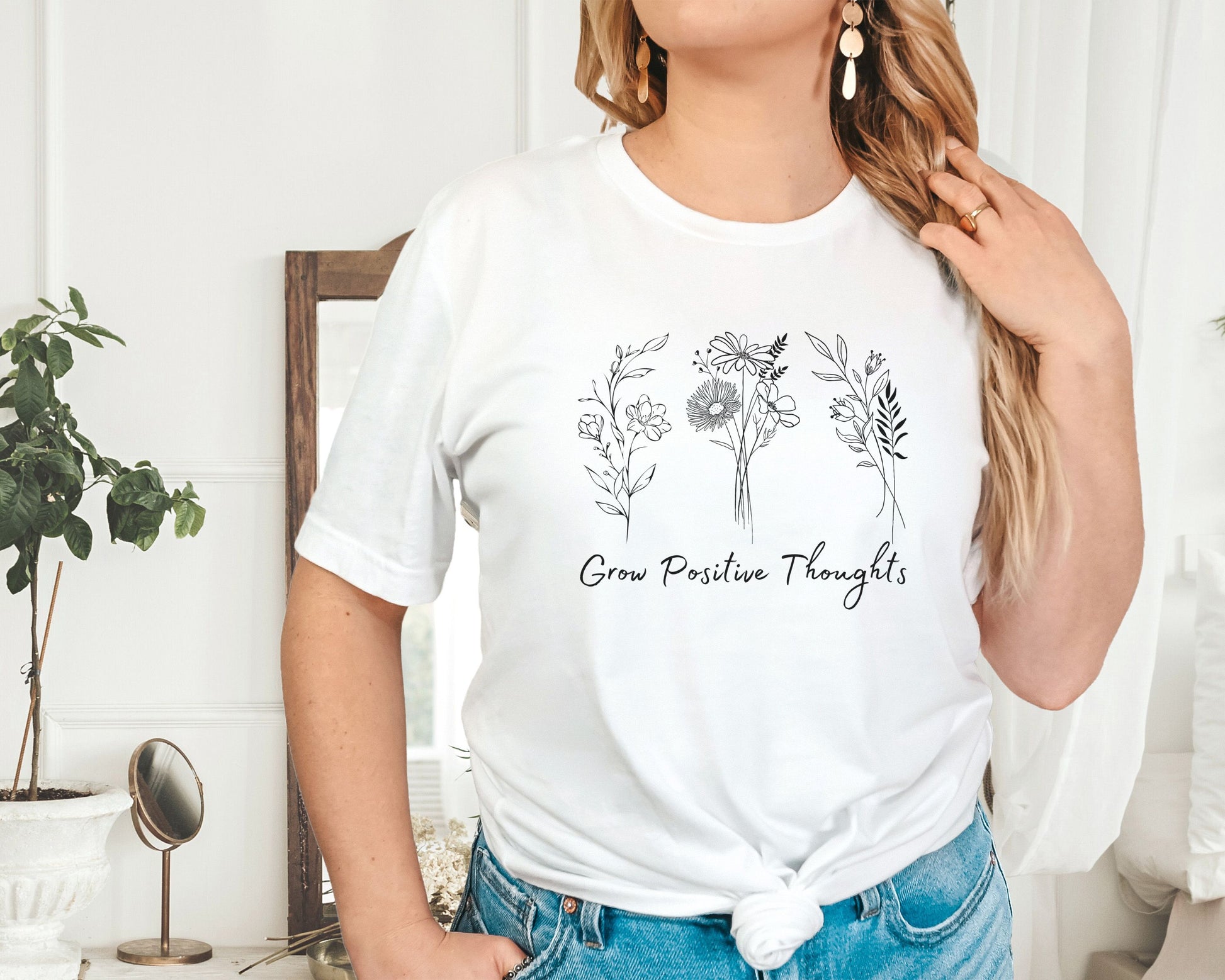 "Grow Positive Thoughts" t-shirt featuring black botanical floral illustrations and an uplifting message in elegant script. Available in white, ash, peach, red, and pink. Soft, lightweight fabric, perfect for spreading positivity and encouragement.