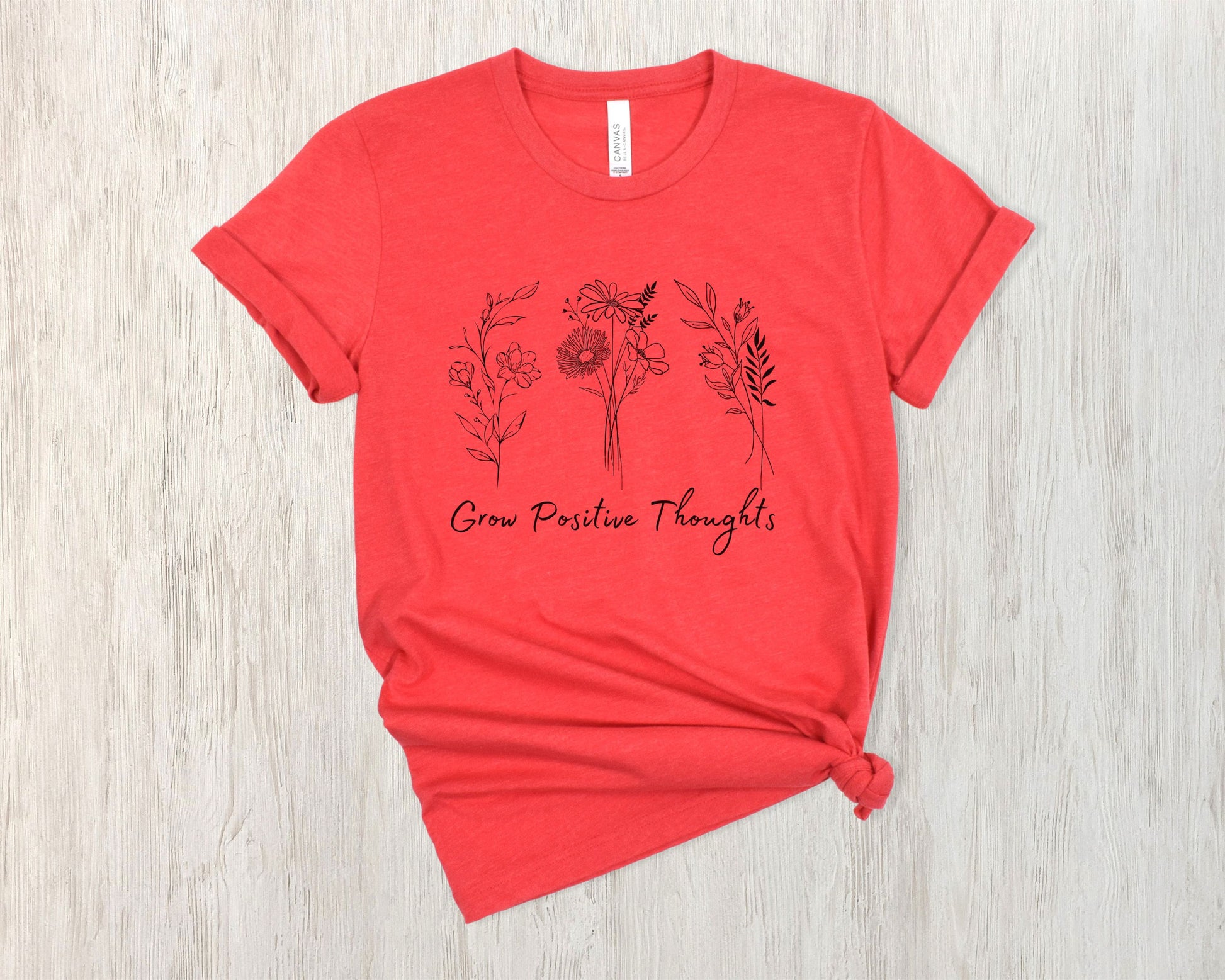 "Grow Positive Thoughts" t-shirt featuring black botanical floral illustrations and an uplifting message in elegant script. Available in white, ash, peach, red, and pink. Soft, lightweight fabric, perfect for spreading positivity and encouragement.