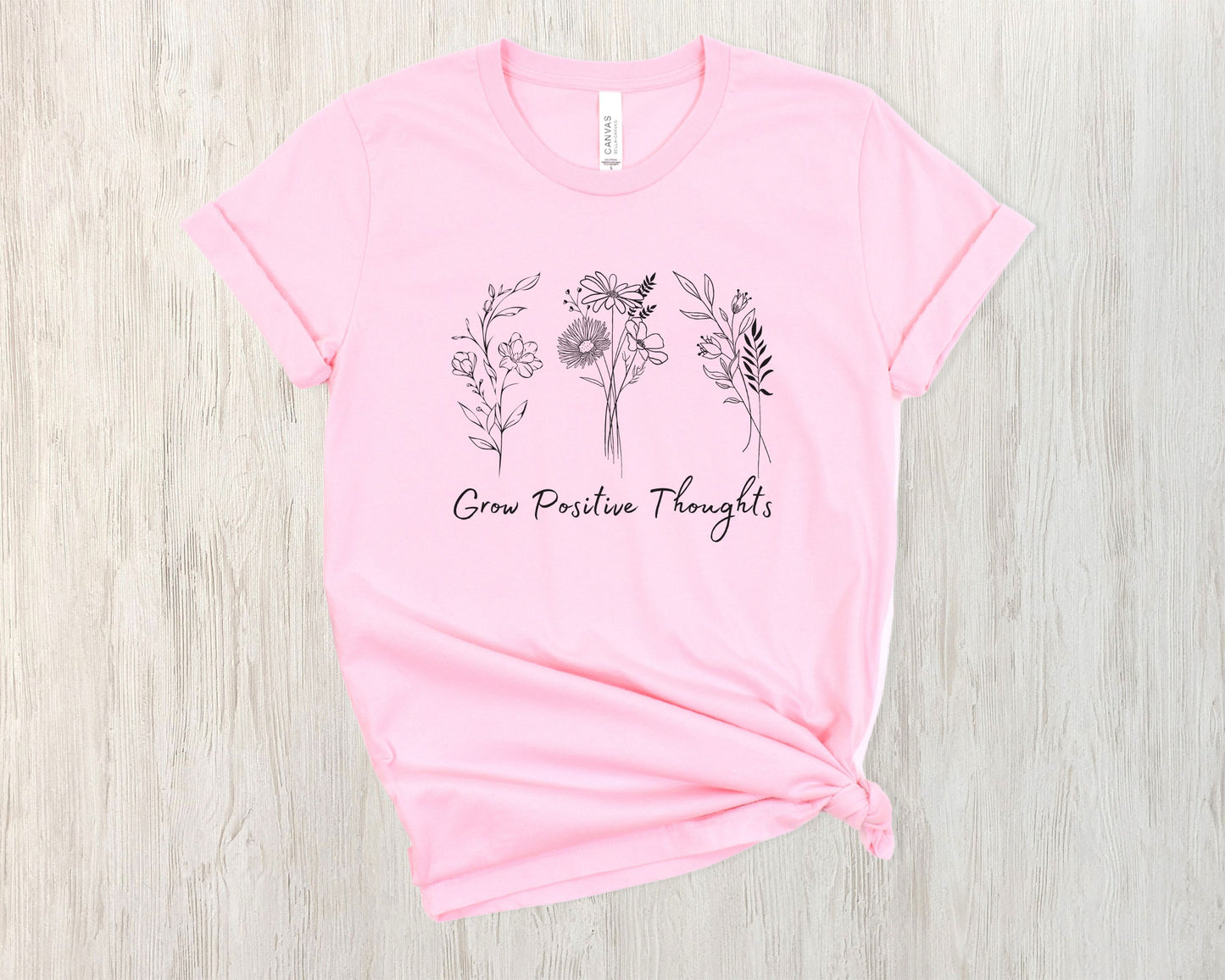 "Grow Positive Thoughts" t-shirt featuring black botanical floral illustrations and an uplifting message in elegant script. Available in white, ash, peach, red, and pink. Soft, lightweight fabric, perfect for spreading positivity and encouragement.