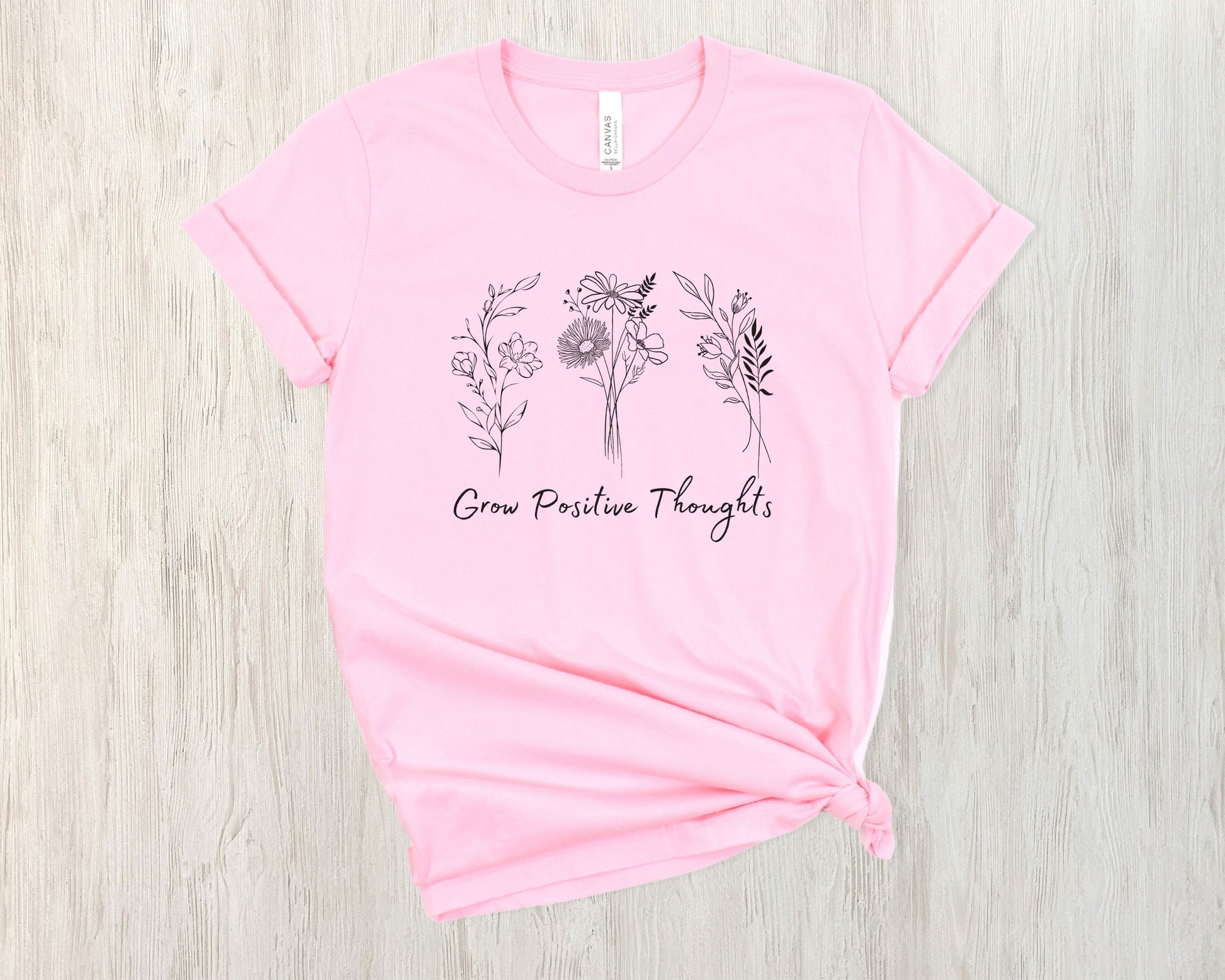 "Grow Positive Thoughts" t-shirt featuring black botanical floral illustrations and an uplifting message in elegant script. Available in white, ash, peach, red, and pink. Soft, lightweight fabric, perfect for spreading positivity and encouragement.
