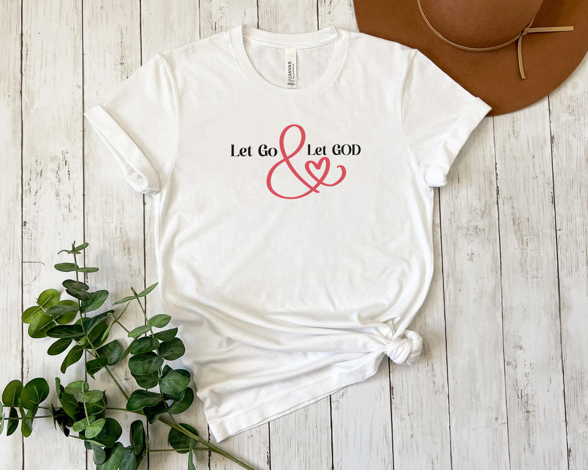 White t-shirt with the phrase ‘Let Go & Let God’ in bold black text and a red ampersand forming a heart. Cozy, inspirational faith-based apparel for everyday wear.