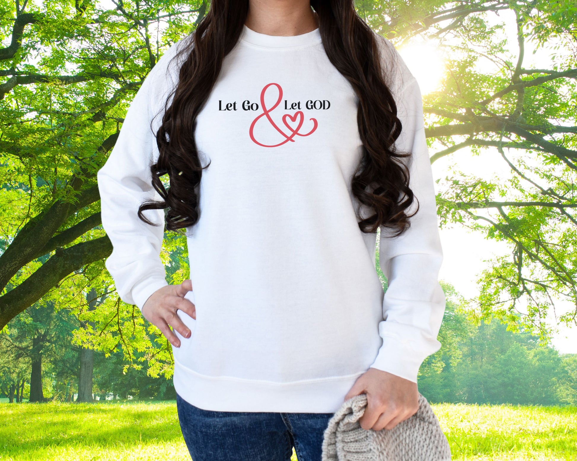 White crewneck sweatshirt with the phrase ‘Let Go & Let God’ in bold black text and a red ampersand forming a heart. Cozy, inspirational faith-based apparel for everyday wear.