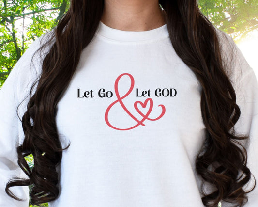 White crewneck sweatshirt with the phrase ‘Let Go & Let God’ in bold black text and a red ampersand forming a heart. Cozy, inspirational faith-based apparel for everyday wear.